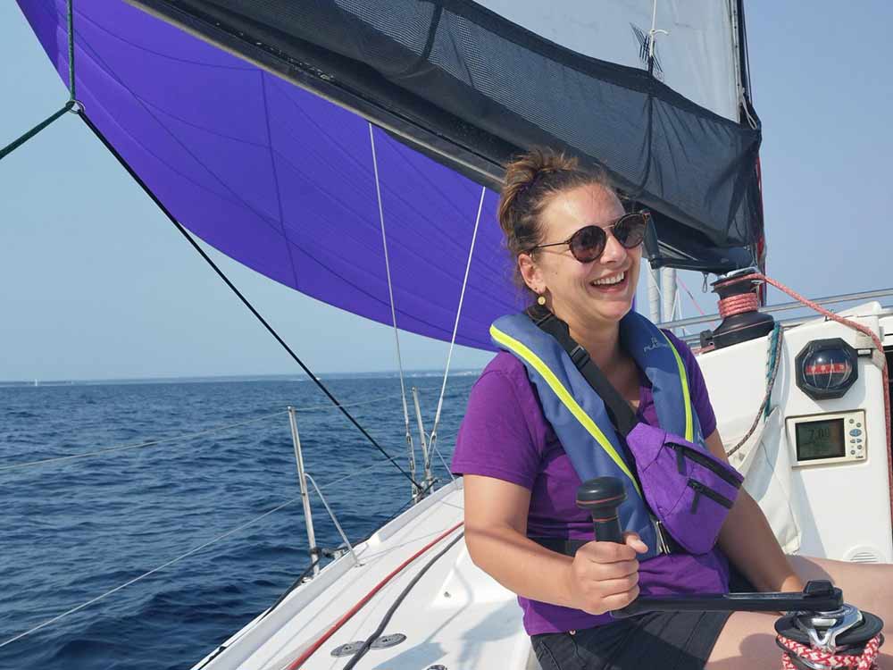 Stagiaire souriante, pose au winch, habillée au couleur du spi sur le Pogo 40